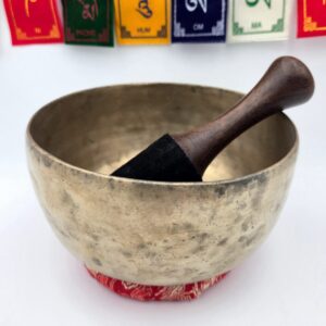 vue de profil bol chantant tibétain antique avec bâton bois cuir sur coussin rouge et drapeaux de prière tibétains en arrière-plan