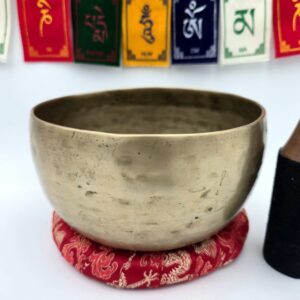 Bol chantant tibétain antique 7 métaux 708 g en Sol – vue extérieure sur coussin rouge avec drapeaux de prière en arrière-plan