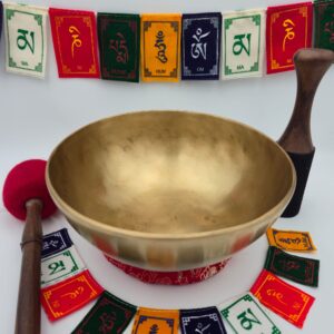 Bol chantant tibétain thérapeutique 7 métaux 1,258 kg en Mi♭ – vue extérieure sur coussin rouge avec bâton bois, mailloche et drapeaux de prière