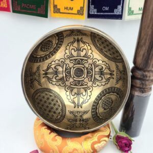 bol tibétain gravé 7 métaux 350 g vue intérieure Double Dorje avec motifs sacrés et coussin orange, bâton bois cuir et drapeaux de prière en arrière-plan