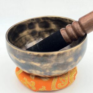 bol tibétain 7 métaux finition matifiée effet léopard, vue latérale avec mailloche noire et coussin orange, ambiance méditation