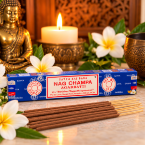 Paquet individuel d'encens indien Satya Nag Champa 15 g devant un Bouddha, une bougie et des fleurs blanches